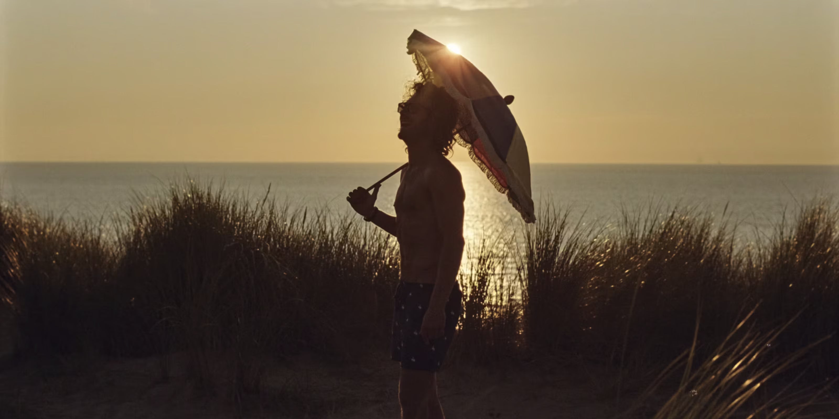 Man holding umbrella by the beach during a sunset