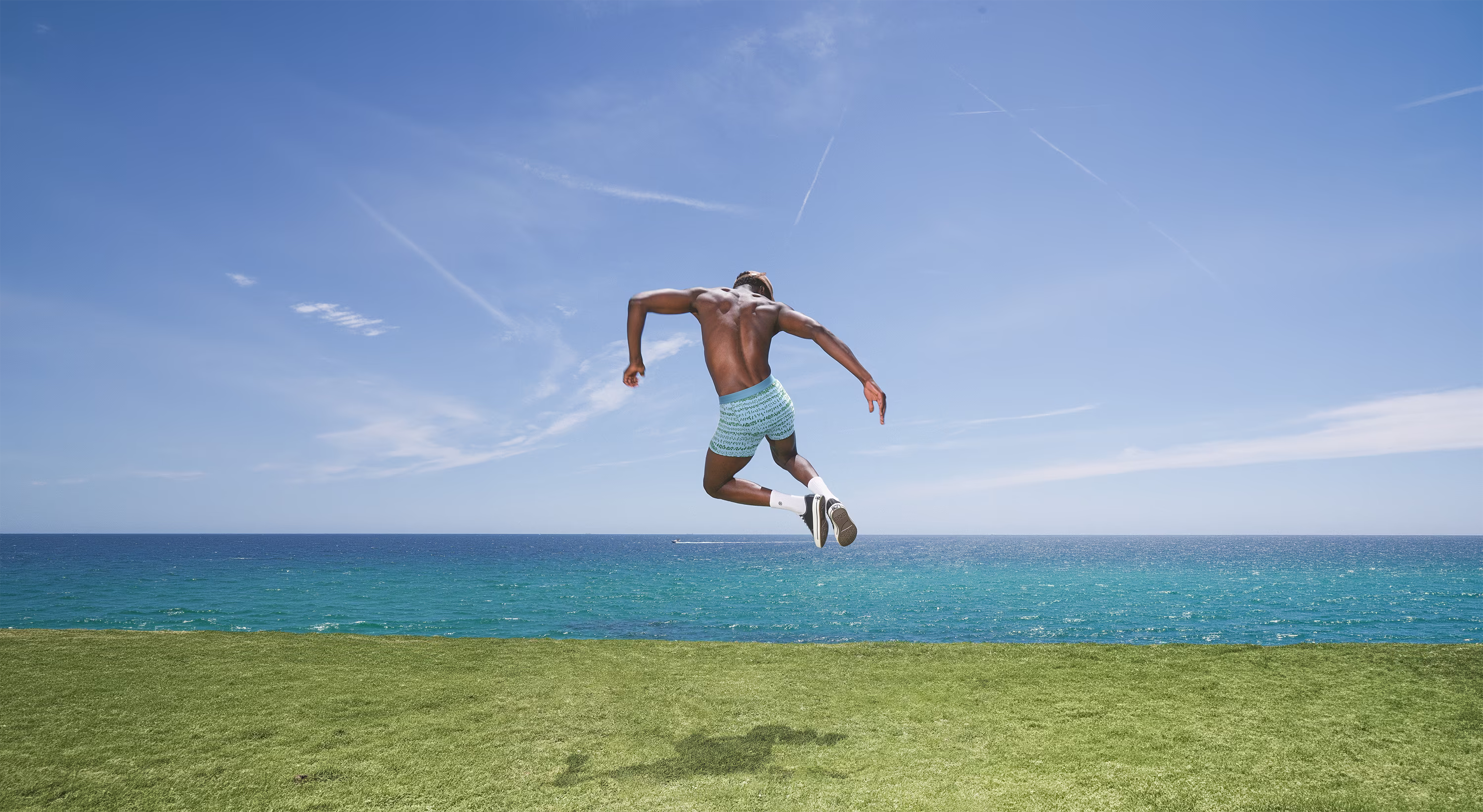 Man jumping on grass with ocean and blue sky in the background